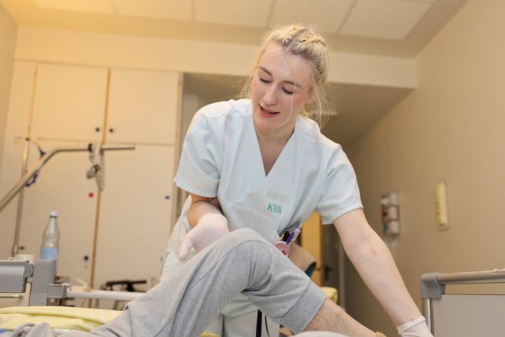 Pflegeschülerin winkelt Bein einer Patientin an